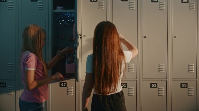 Blonde Schoolgirl Organizes Decorated Locker, Reaching in to Grab Pink Notebook before Class, while Brunette Friend Stands Beside in School Corridor. Educational Lifestyle and Daily School Routine.