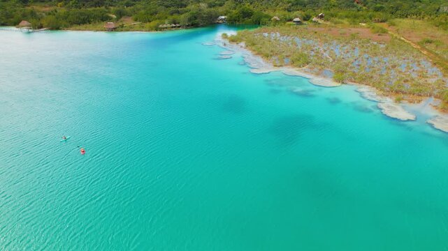 Aerial view of blue Bacalar Lagoon with kayakers and tropical shore of Mexico