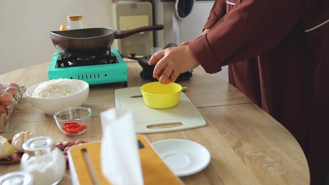 Hands breaking fresh chicken egg yolk into bowl with fork to prepare fried rice in home kitchen