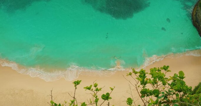 Ocean waves wash over sand at the base of cliffs on Nusa Penida Island Bali