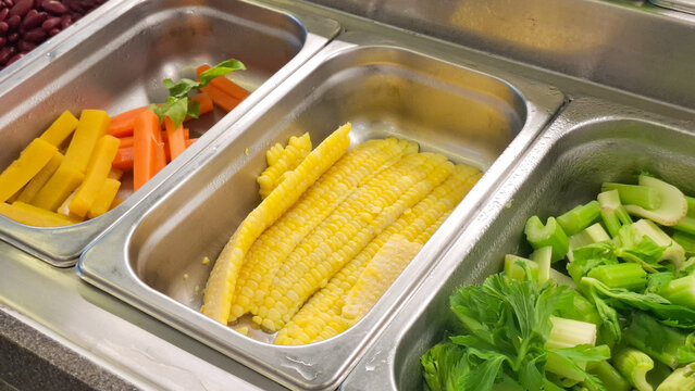 Selection Of Fresh Salad Bar Ingredients Featuring Baby Corn Celery And Carrots In Stainless Steel Metal Trays
