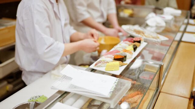 Professional sushi chef preparing nigiri and sashimi platter in authentic japanese restaurant kitchen.