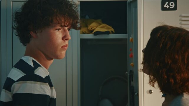 In Hallway Angry Teenage Girl Aggressively Grabs Male Classmate By Collar Of T Shirt. Boy Looks Shocked While Girls Corner Against Metal Lockers. Physical Abuse, Teenage Rage, And High School Assault.