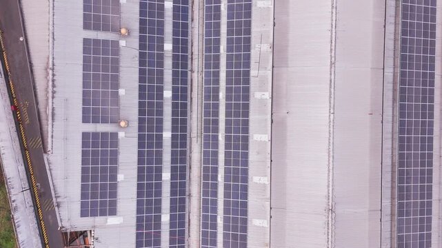 Aerial drone view of a large industrial complex in Indonesia with extensive solar panels installed across factory rooftops. The geometric arrangement of buildings, photovoltaic panels, roads, and surr