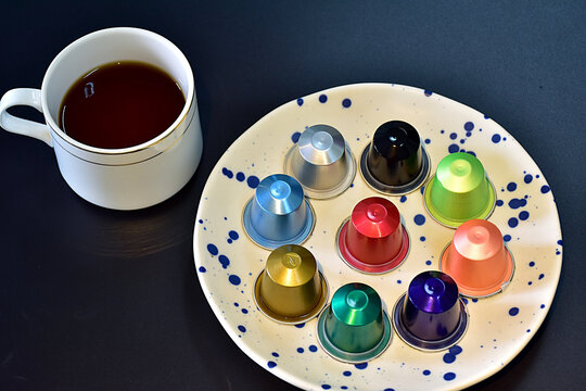 Cup of coffee with colorful coffee capsules on ceramic plate