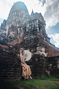 Portrait of Asian teenage girl tourist dressed in traditional Thai outfit with cheerful smile at old brick castle, holiday travel in Ayutthaya palace, ancient ruins heritage,  travel destination.