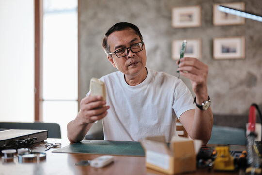 Mature Asian man checks and compares spare parts parcel, air conditioner remote control circuit board replacement, home electrical appliance fix, electronics component hobbyist, enthusiast workshop.
