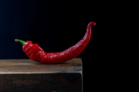 Red chili pepper on wood block against black background