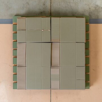 Flattened corrugated cardboard boxes stacked in an organized grid on a muted green pallet, featuring a matte texture for shipping and returns backgrounds