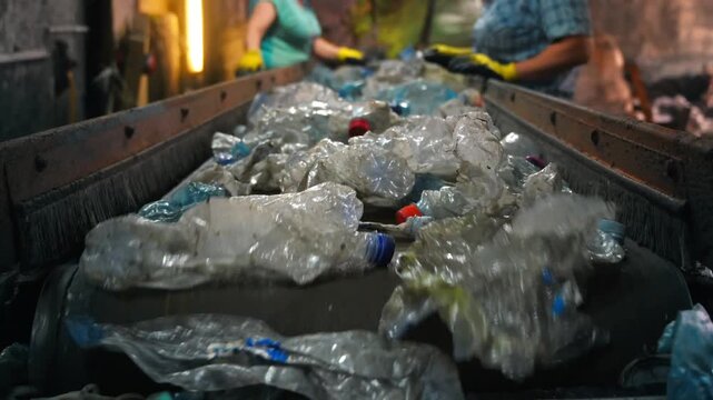 Industrial conveyor belt moving plastic waste for recycling at processing facility with workers sorting materials.