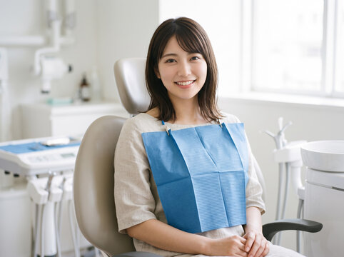 歯科医院で治療用のエプロンをつけて診察台に座り笑顔を見せる女性