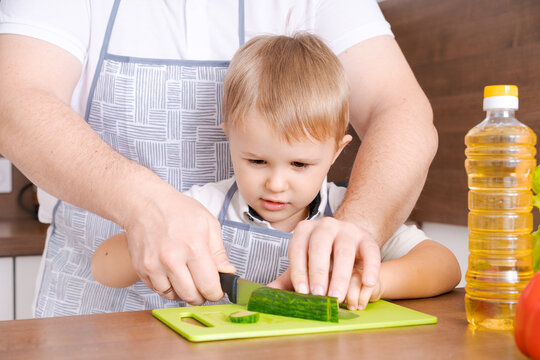 Focused caucasian toddler boy watching a cucumber being cut on a green board, ideal for child development, early learning and motor skills content