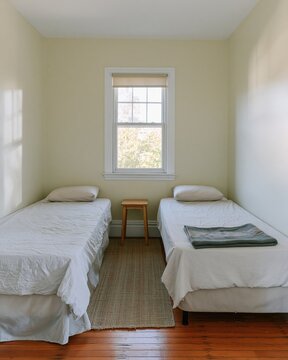 Compact twin bedroom with two single beds and muted sage green walls, featuring lived-in linen textures for rental listings and small space living