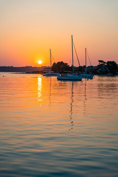 Sailing yachts anchored in a calm bay during a colorful summer sunset over the sea. Peaceful evening, golden hour, coastal travel destination and relaxing sailing lifestyle.