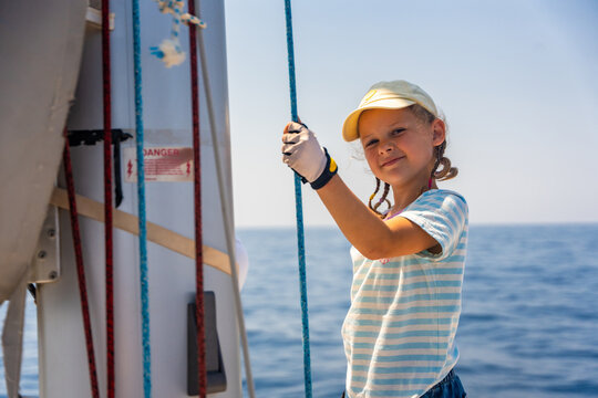 Smiling young girl holding a sailing rope on a family yacht during a sea voyage. Learning sailing skills, building confidence, independence and outdoor adventure through real experience.