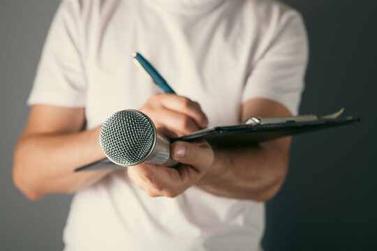 Man hand holding microphone and writing on clipboard on gray background, closeup