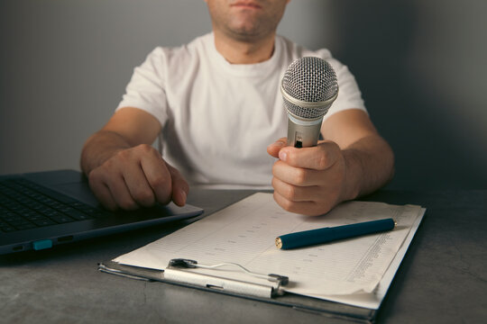 Man hand holding microphone and writing on clipboard on gray background, closeup
