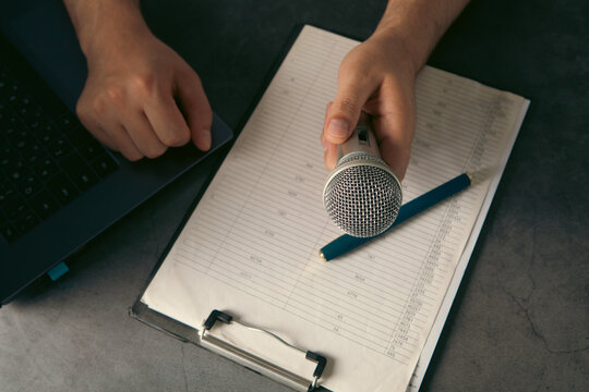 Man hand holding microphone and writing on clipboard on gray background, closeup