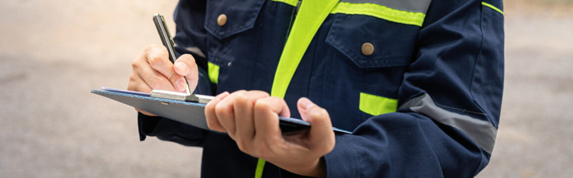 A safety officer is checking on hazardous chemical material checklist for risk assessment before tranportation the dangerous good with train tanker railway background. Industrail working scene.