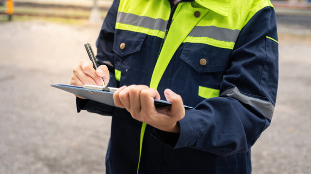 A safety officer is checking on hazardous chemical material checklist for risk assessment before tranportation the dangerous good with train tanker railway background. Industrail working scene.