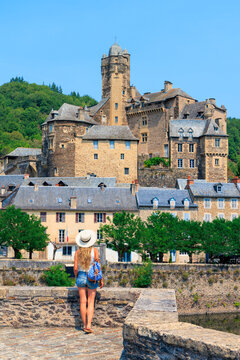 full length view of female tourist standing on historic stone bridge admiring medieval french castle, Estaing in Aveyron
