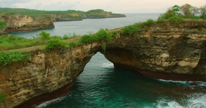Scenic rock formation ocean archway bridge nature landscape with lush greenery in Broken Beach Bali Indonesia