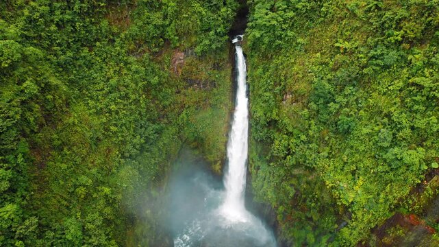 Aerial view of a tall rainforest waterfall plunging into a pool in Costa Rica