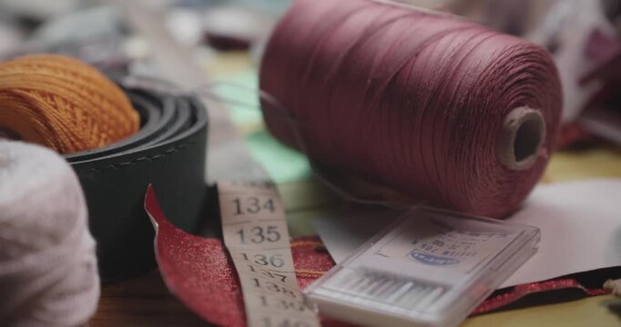 A slow slide reveals a collection of colorful yarns, zips, and essential haberdashery items on a professional tailor sewing workspace.