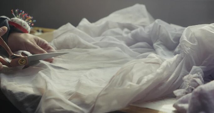 Close-up of a fashion designer cutting white semi-transparent tulle fabric on a studio worktable, highlighting precision dressmaking and textile craftsmanship.