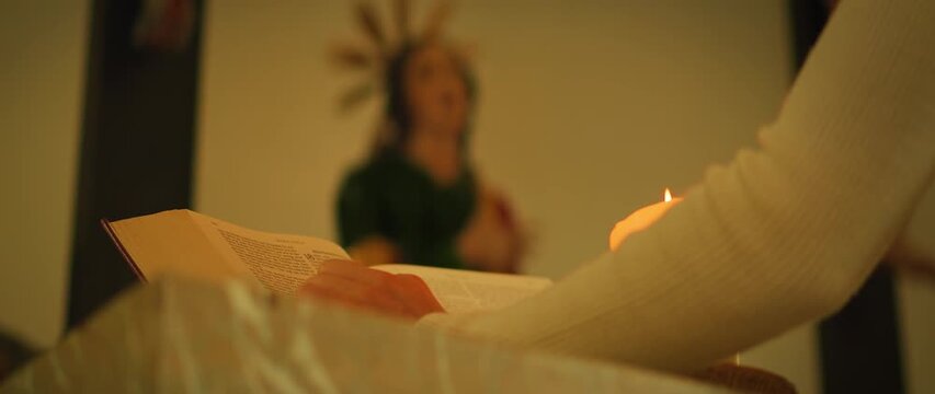 Woman reading Bible by candlelight in church with Virgin Mary on background