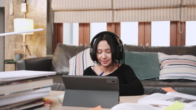 Asian teenage girl concentrates on online class, remote learning at home using tablet, writing and reading textbooks, self-study for back to school, Homeschooling, university education lifestyle.