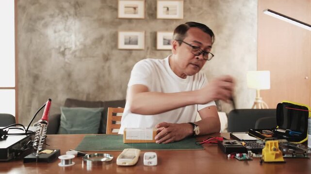 Mature Asian man unboxing delivery parcel order, air conditioner remote control circuit board spare parts, home electrical appliance repair, electronics component hobbyist, enthusiast skill workshop.