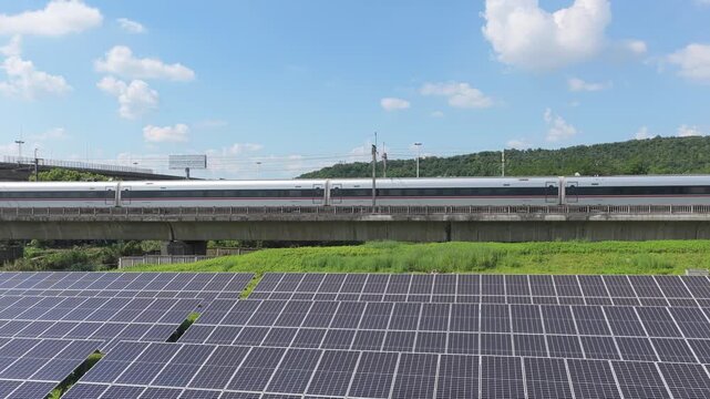 High speed train passing solar panels beside a highway