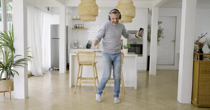 Joyful senior caucasian man person dancing listen to music in a bright modern living space, enjoying music, movement, carefree pension retire male relaxation at home.