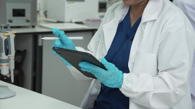 Scientist in a lab coat and gloves using a tablet computer while working in a modern laboratory