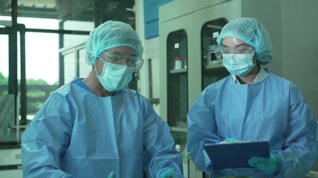 Two healthcare workers in protective gear handling lab equipment and taking notes in a clinical setting