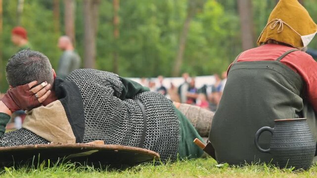 medieval reenactors relax on the grass, dressed in authentic clothing typical of the early Middle Ages