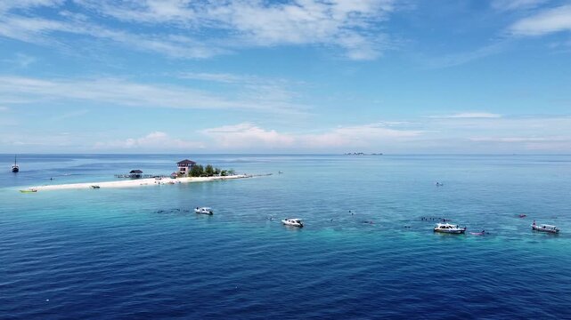 Aerial drone video moving forward and orbiting a small tropical island with white sand, turquoise sea water, and tourist boats in Makassar, Indonesia
