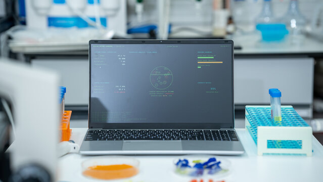 Laptop displaying lab data on a bench with test tubes and samples in a modern science laboratory