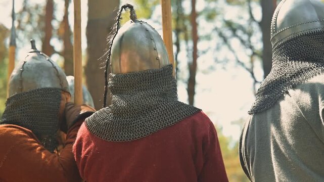 viking men dressed in armor participate in training while surrounded by trees. The activity takes place outdoors in a natural setting during daytime, focusing on teamwork and skill development
