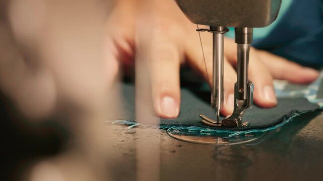 Close-up of a mechanical sewing machine needle and presser foot stitching dark fabric while hands carefully guide the material, showing precision tailoring and craftsmanship.