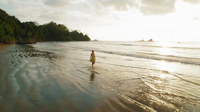 Woman in summer dress walking on sandy shore of Dominicalito Beach Costa Rica