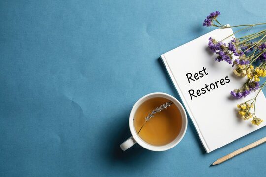 White notebook with rest restores text, tea cup, and dried flowers on blue background