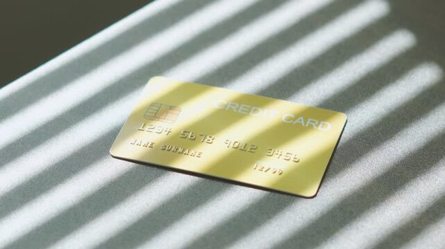 Financial decision online transaction, gold credit card dropping down on surface with striped window light.