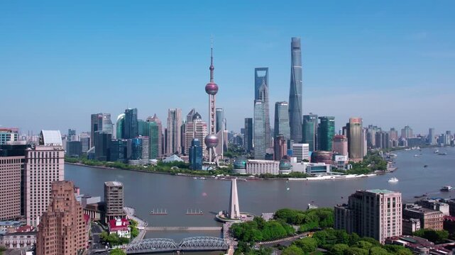 A panoramic urban skyline of modern high-rise buildings along a wide river under a clear blue sky on a bright day.