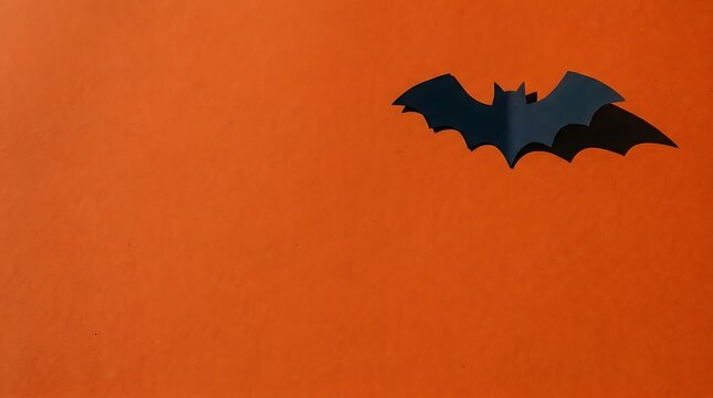Black paper bat silhouette on a vibrant orange background for