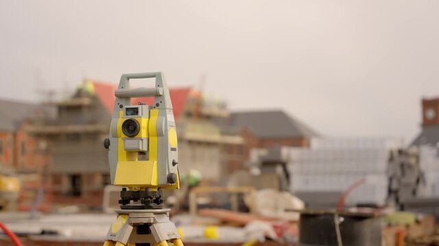 Surveying work takes place at a construction site with survey equipment set up in the foreground
