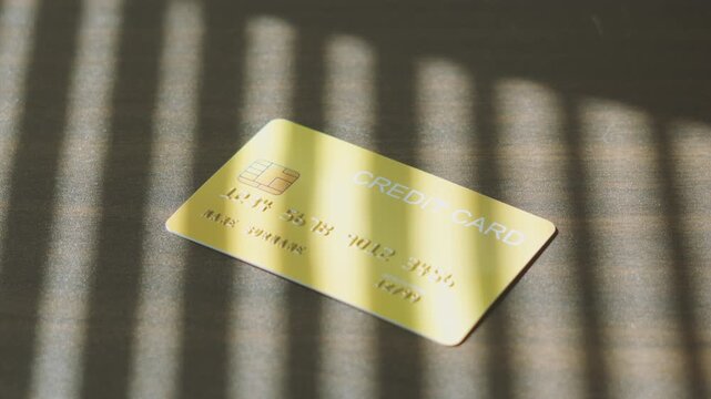 Secure online transaction, gold credit card dropping down on surface with striped window light.