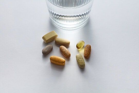 Dietary Supplements, Vitamin Pills and Glass of Water on White Background