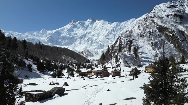 Winter aerial scene of Fairy Meadows base camp nestled among pine trees and deep snow beneath towering peaks in Hunza Valley, Pakistan adventure travel destination